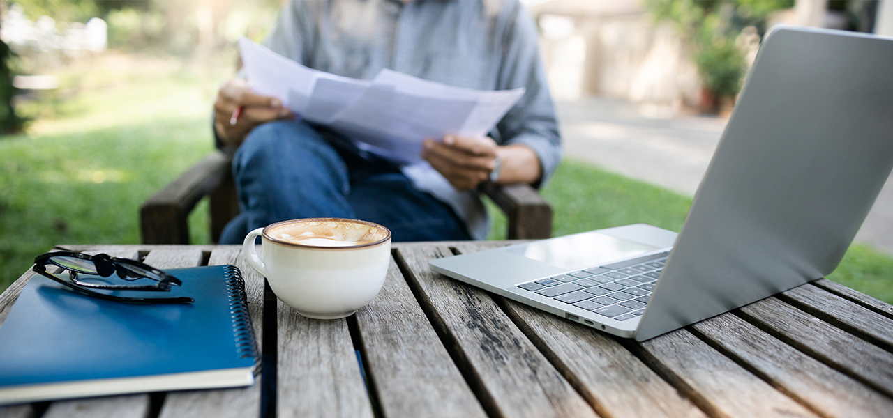 Person working outside on a laptop on a sunny day reviewing papers.