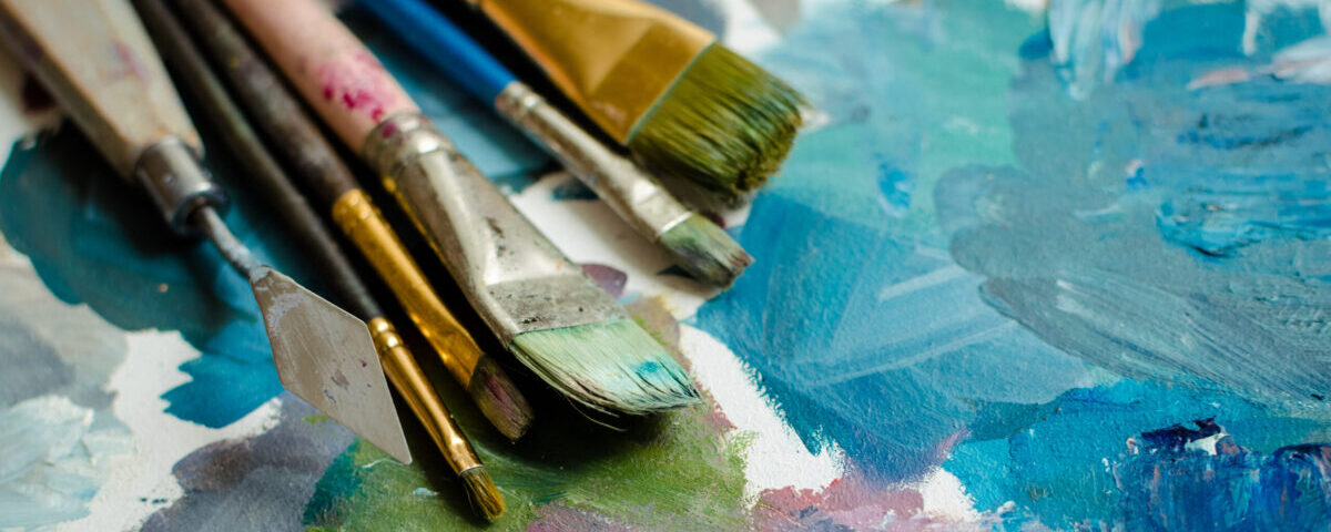 Paint brushed on a painted canvas with blue and green paints.