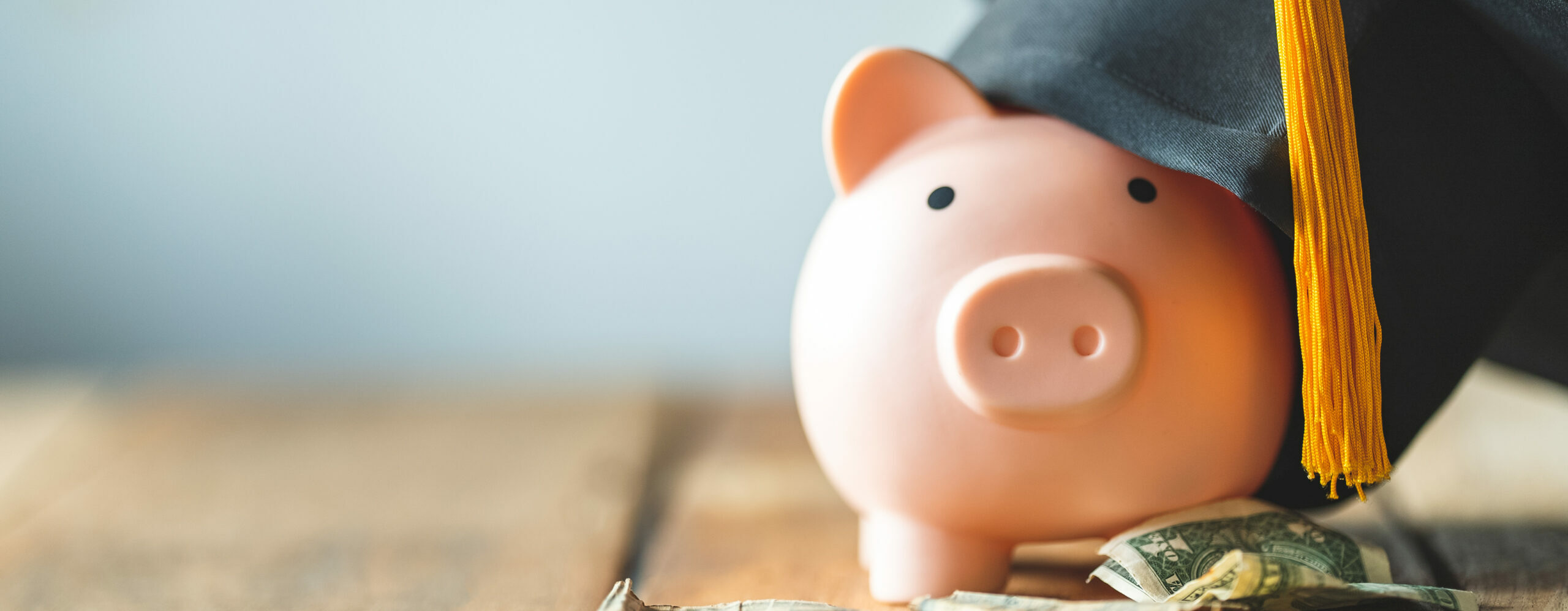 piggy bank with graduation cap on old wood with paper money and coins.