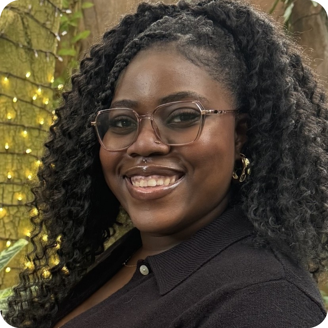 Smiling Black woman with curly hair and glasses outdoors, warm fairy lights in the background.
