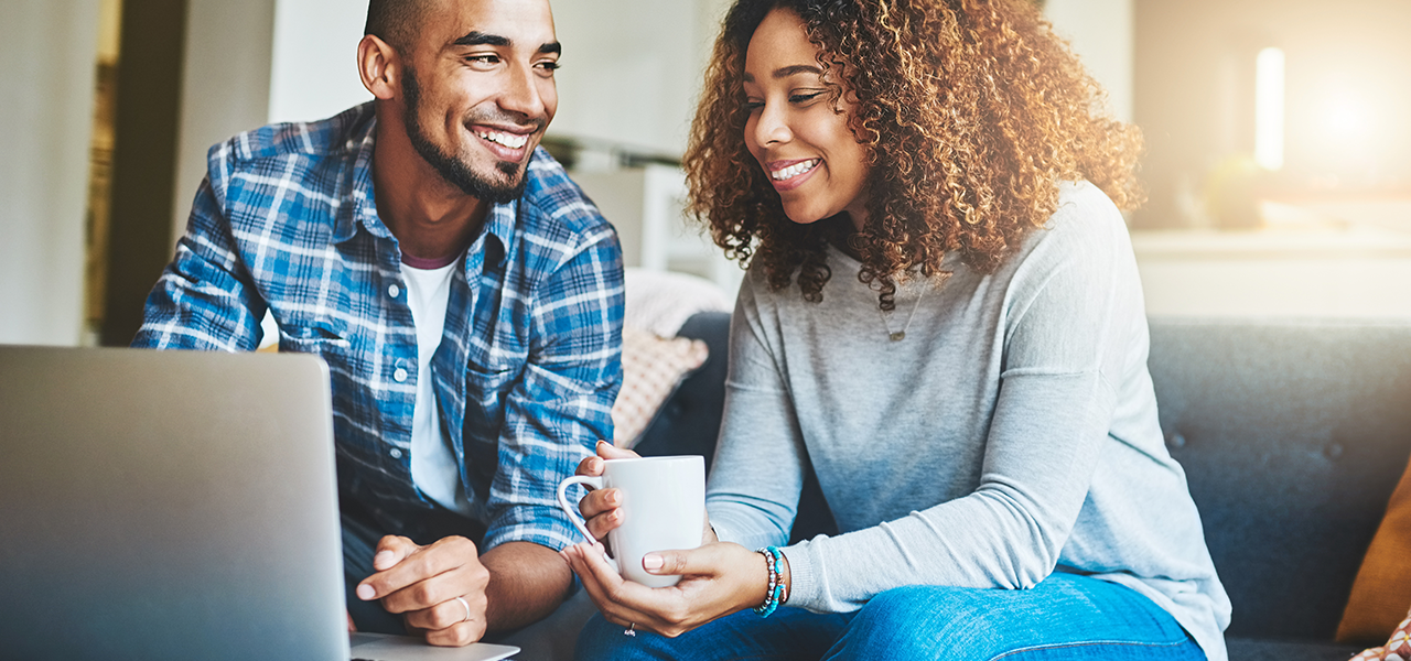 Downloaded File #: 522937765 Home finance, savings and investment with a young couple working on a laptop in their living room. Man and woman calculating a household budget together while relaxing and drinking coffee on the sofa